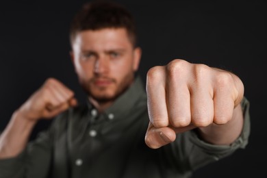 Photo of Young man ready to fight against black background, focus on hand. Space for text