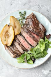 Pieces of delicious roasted beef meat, caramelized pear and greens on light textured table, top view