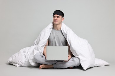Photo of Happy man in pyjama wrapped in blanket using laptop on grey background