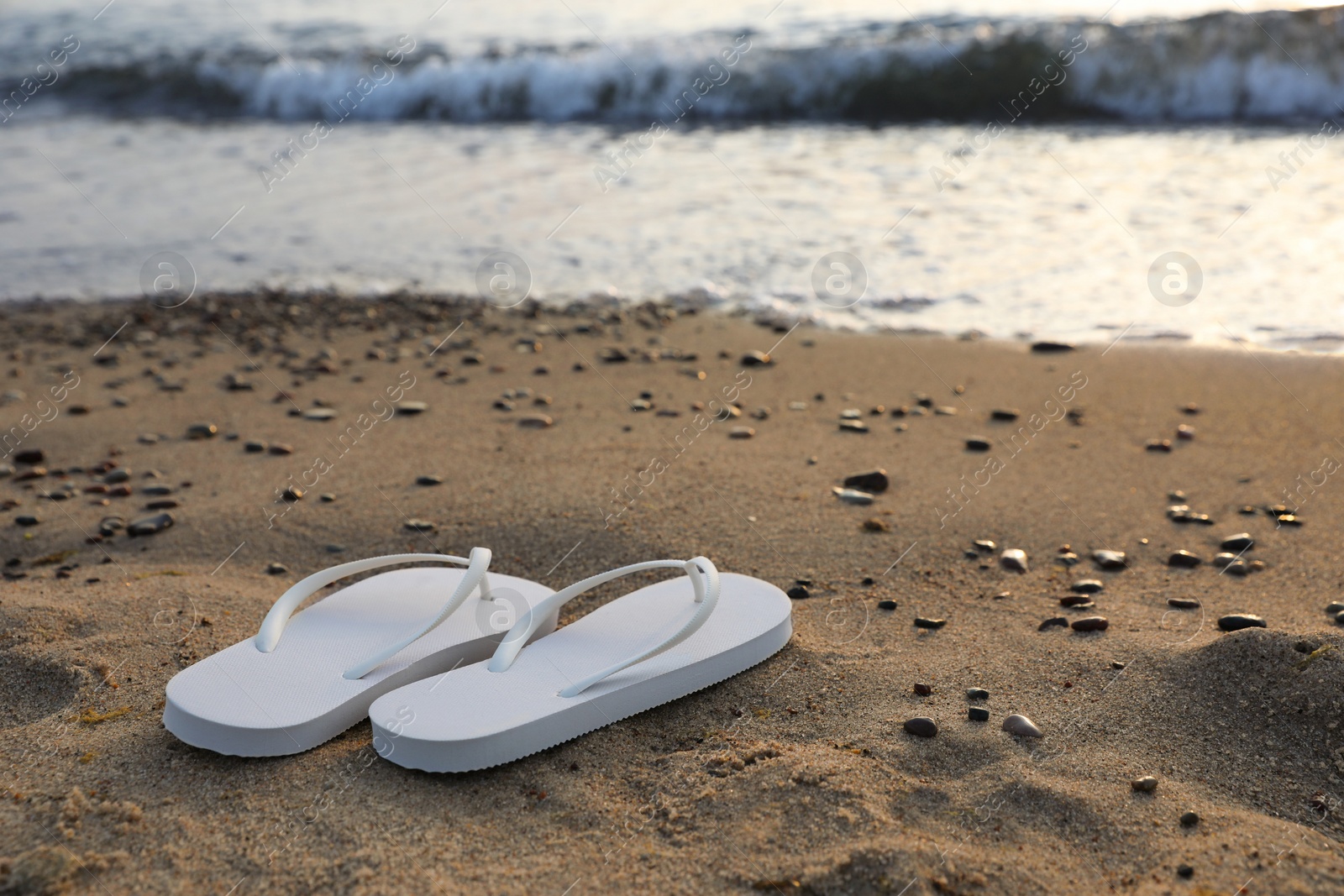 Photo of Stylish white flip flops on sand near sea. Space for text