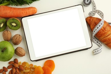 Tablet with blank screen, measuring tape and products on white table, flat lay