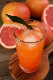 Photo of Tasty grapefruit drink with ice in glass and fresh fruits on wooden table, closeup
