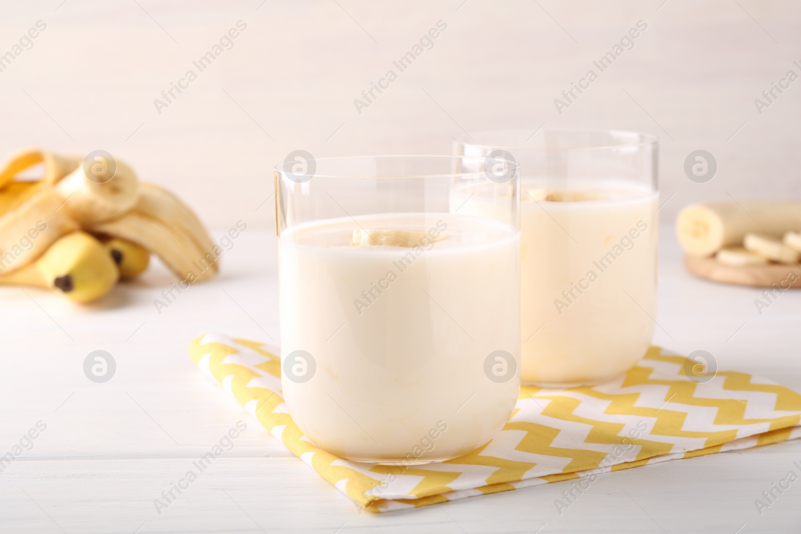 Photo of Tasty yogurt and banana in glasses on white wooden table, closeup