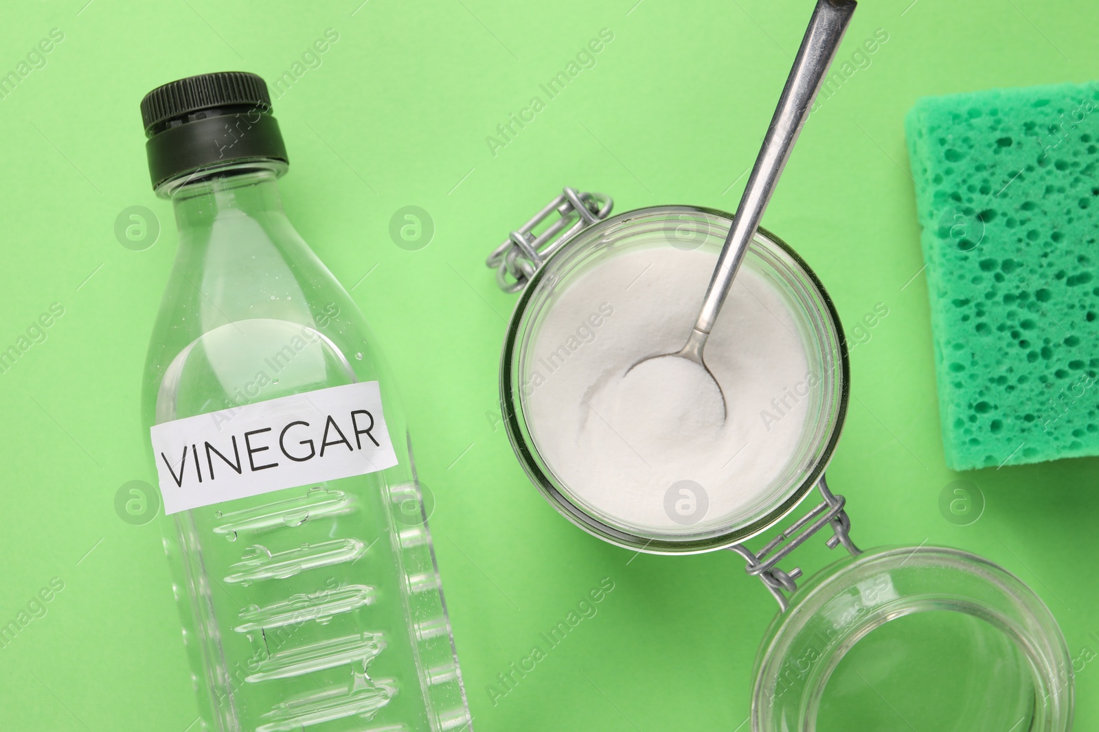 Photo of Eco friendly natural cleaners. Vinegar in bottle, sponge and jar of soda on green background, flat lay