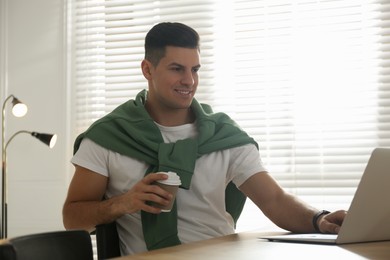 Photo of Freelancer with cup of coffee working on laptop at table indoors