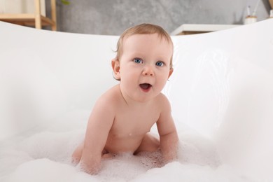 Photo of Cute little baby taking foamy bath at home
