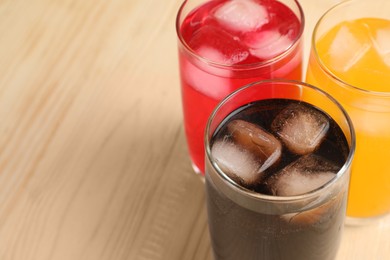 Glasses of different refreshing soda water with ice cubes on wooden table, closeup. Space for text