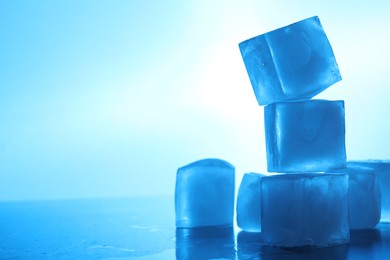 Photo of Crystal clear ice cubes on light blue background, space for text. Color tone effect