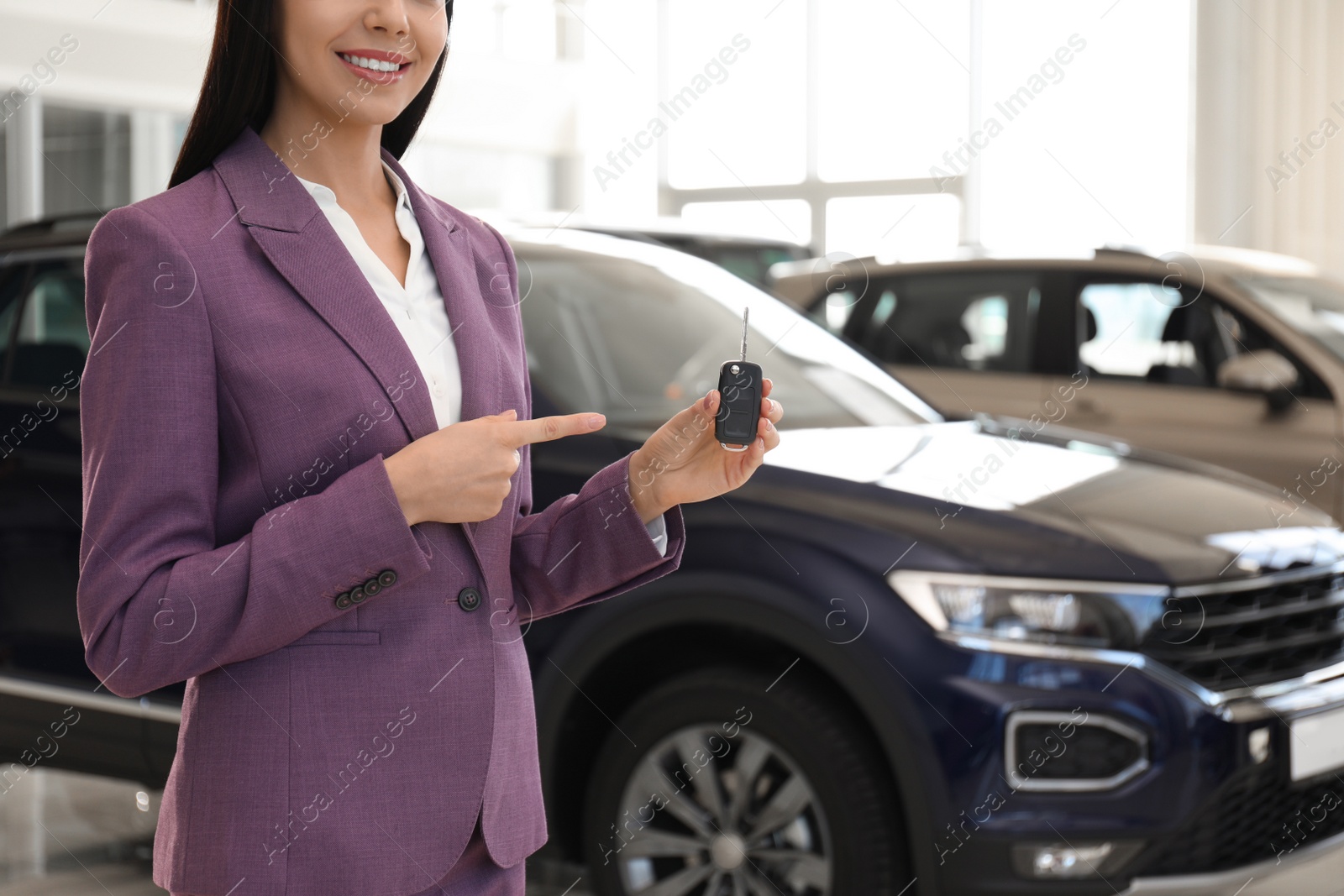 Photo of Saleswoman with key in modern car salon, closeup