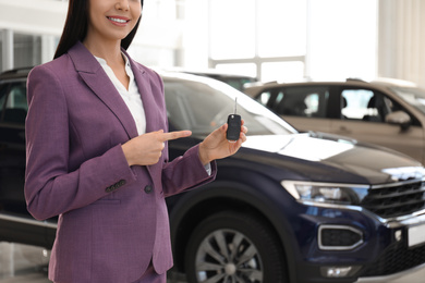 Photo of Saleswoman with key in modern car salon, closeup