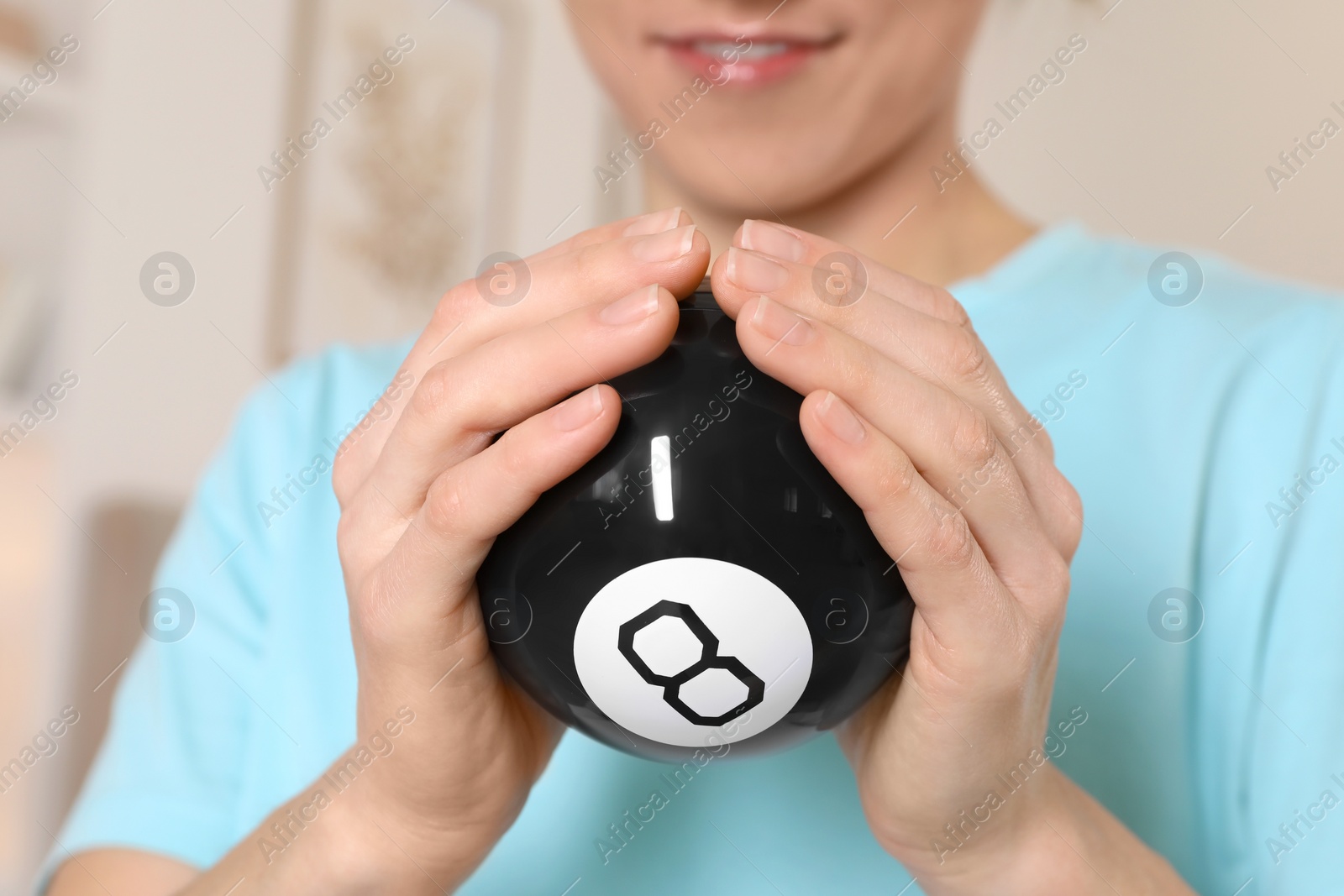 Photo of Woman holding magic eight ball indoors, closeup