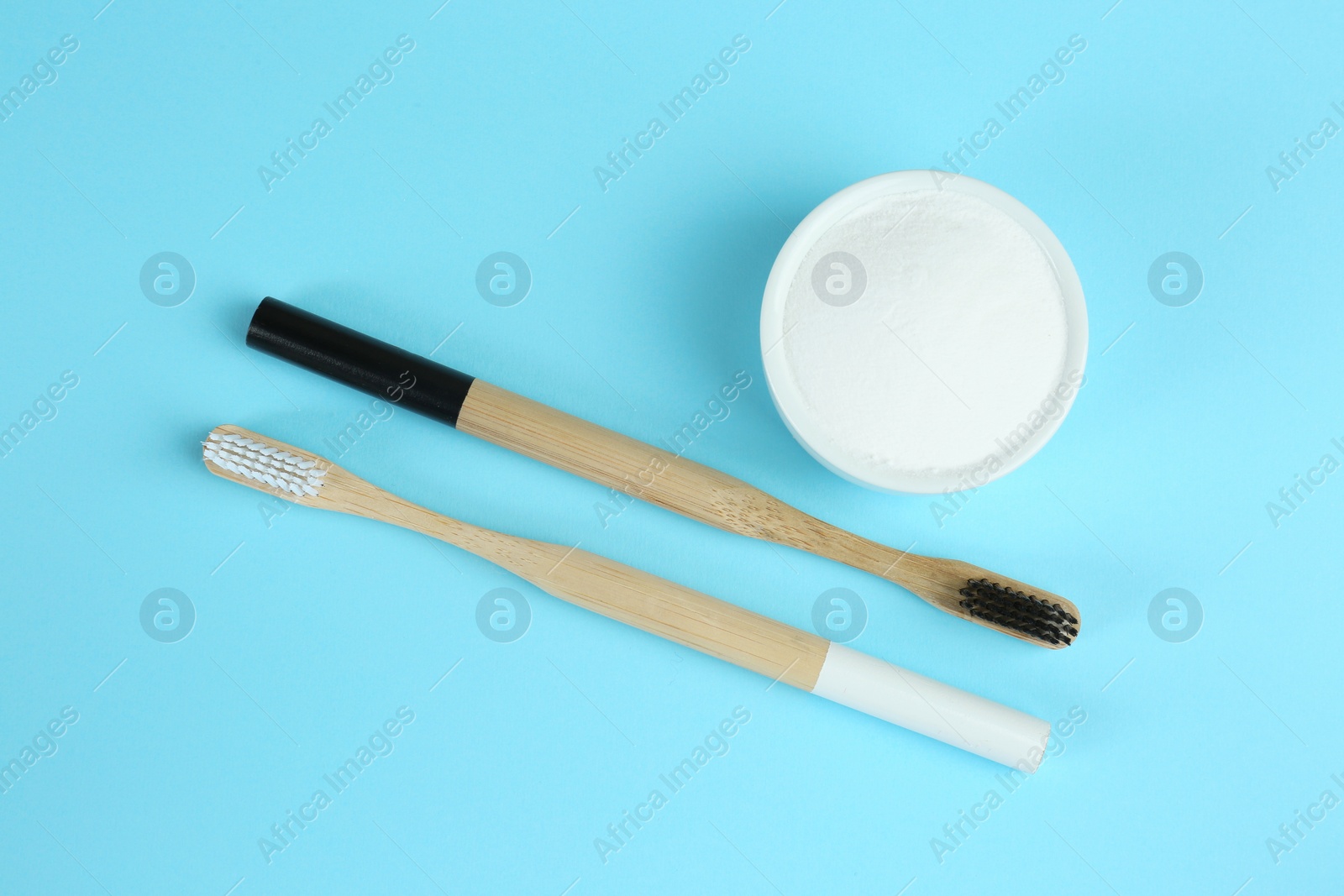 Photo of Bamboo toothbrushes and bowl with baking soda on light blue background, flat lay