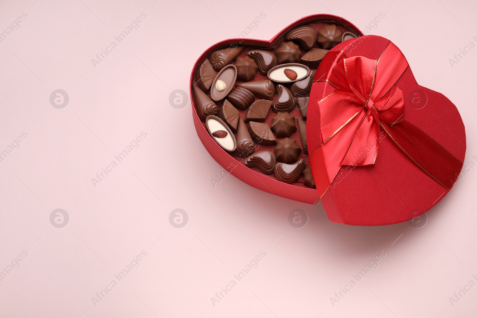 Photo of Heart shaped box with delicious chocolate candies on pale pink background, top view. Space for text
