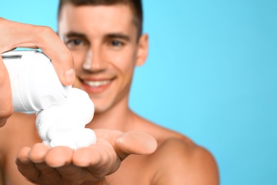 Photo of Handsome young man with shaving cream on light blue background, closeup view. Space for text
