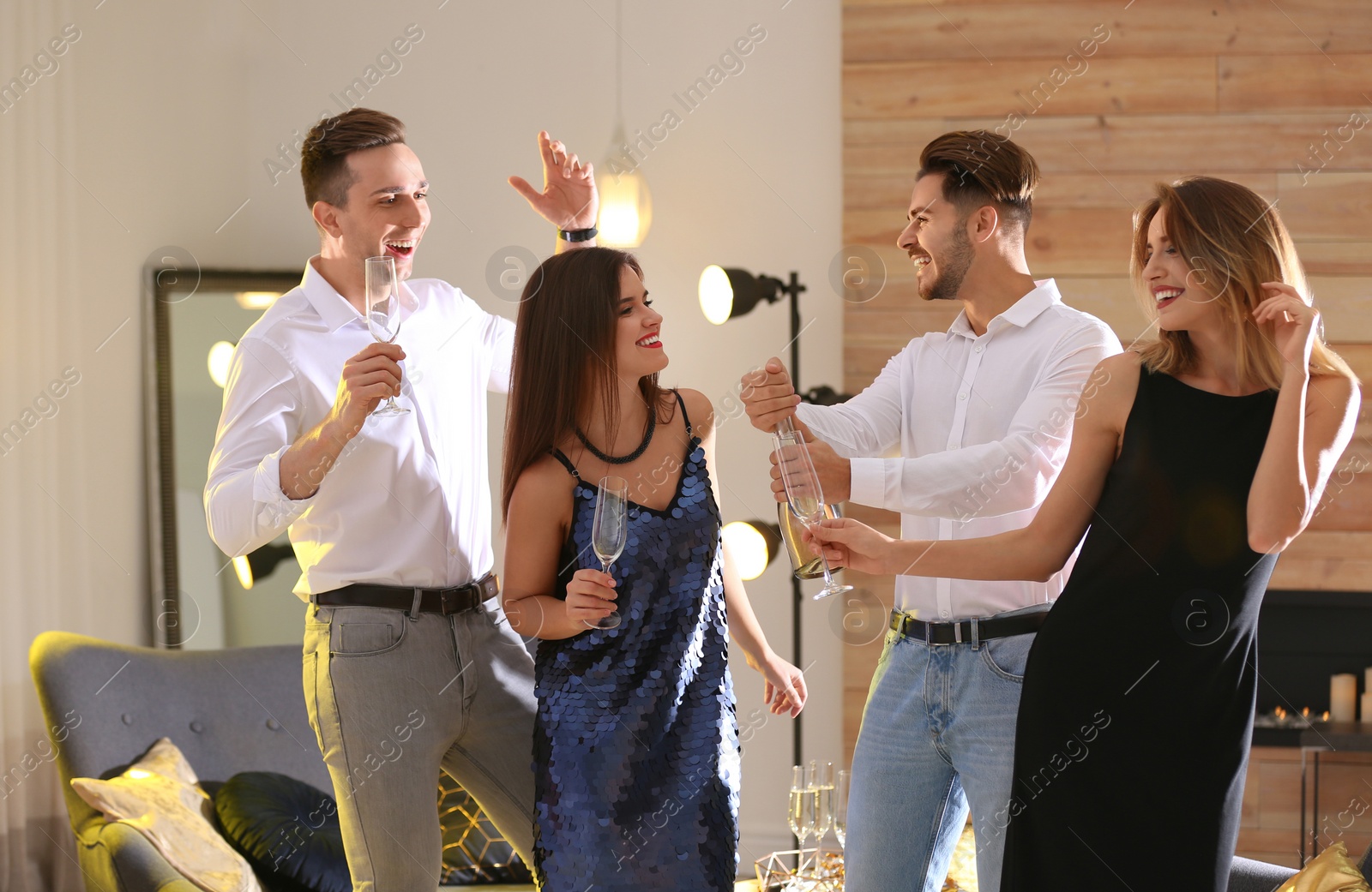 Photo of Man opening bottle of champagne among friends at party indoors