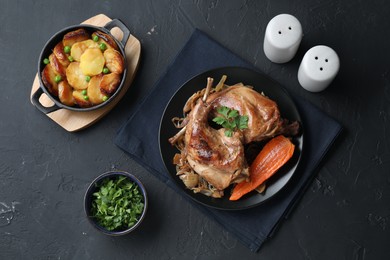 Tasty cooked rabbit meat with vegetables and potato served on black table, flat lay