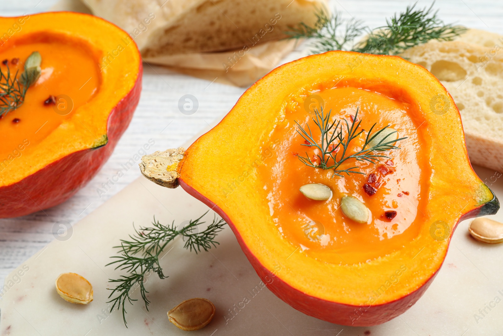 Photo of Tasty cream soup in pumpkin half on white wooden table