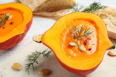 Photo of Tasty cream soup in pumpkin half on white wooden table