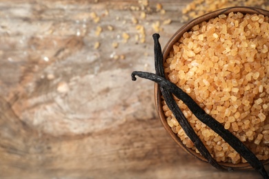 Photo of Bowl of aromatic vanilla sugar and sticks on wooden background