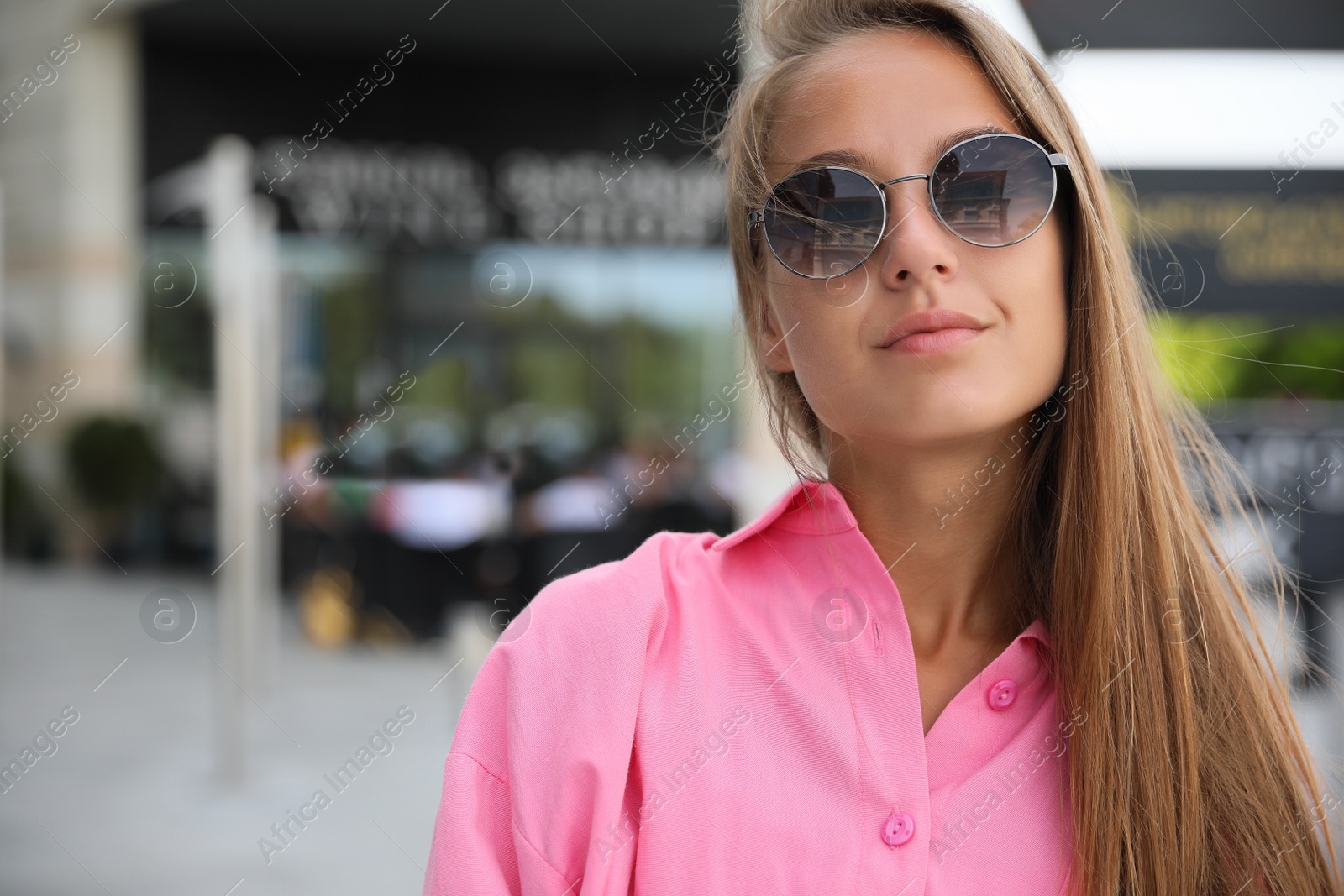 Photo of Beautiful young woman in stylish sunglasses on city street, space for text