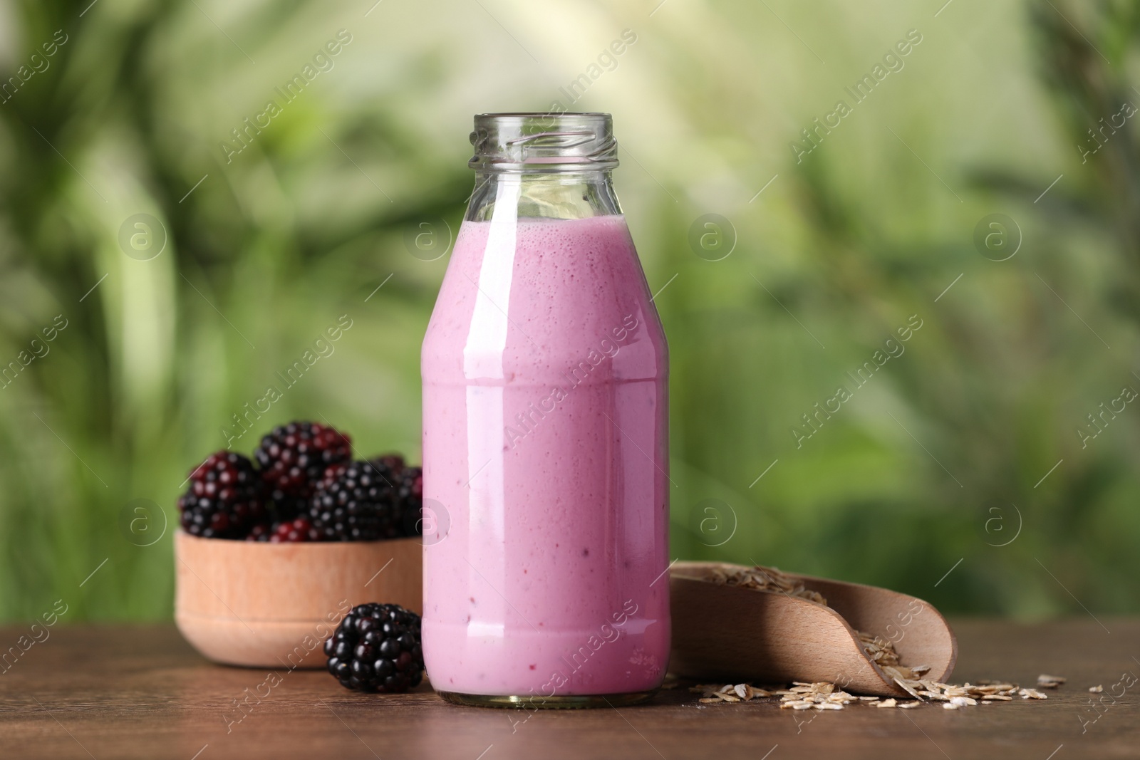 Photo of Delicious blackberry smoothie in glass bottle, oatmeal and berries on wooden table