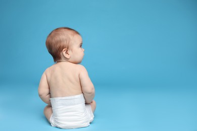 Photo of Cute little baby in diaper sitting on light blue background. Space for text