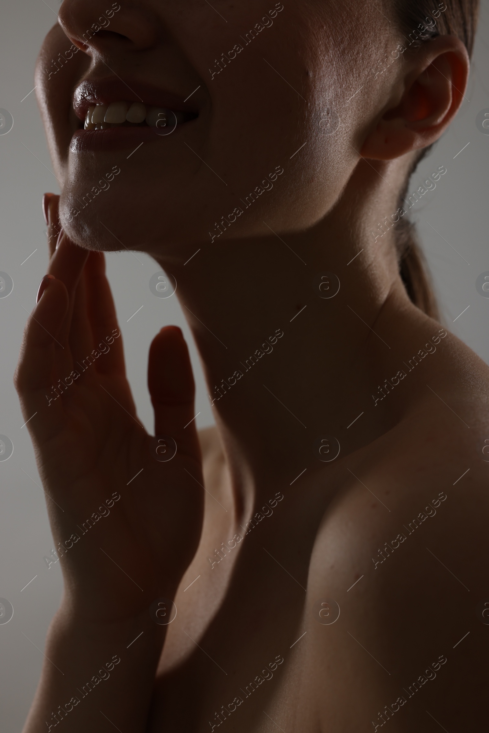 Photo of Smiling woman touching her chin on grey background, closeup
