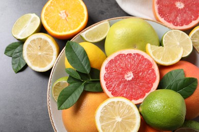 Photo of Different fresh citrus fruits and leaves on grey textured table, flat lay