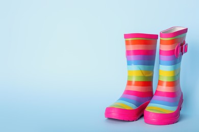 Photo of Pair of striped rubber boots on light blue background. Space for text