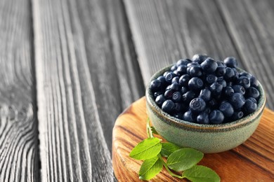 Bowl of tasty fresh bilberries and green leaves on wooden table, closeup. Space for text