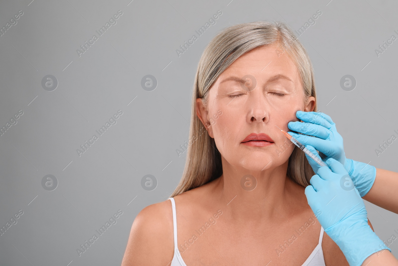 Photo of Doctor giving facial injection to senior woman on light grey background, closeup and space for text. Cosmetic surgery