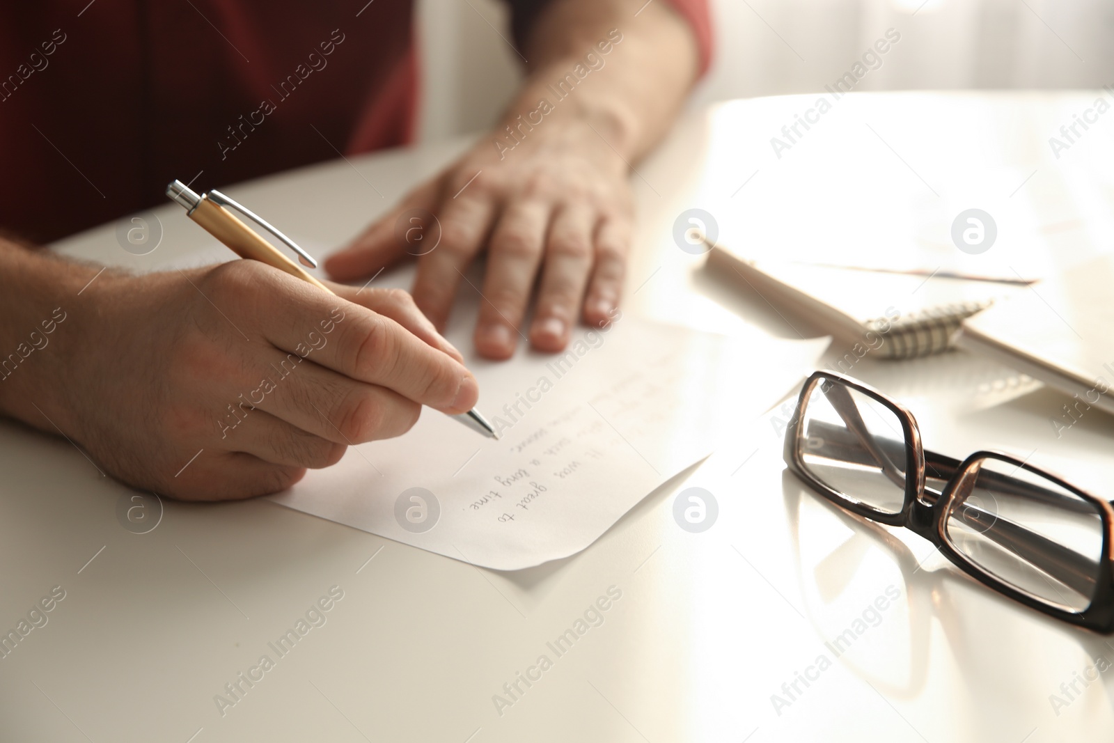 Photo of Man writing letter at white table in room, closeup