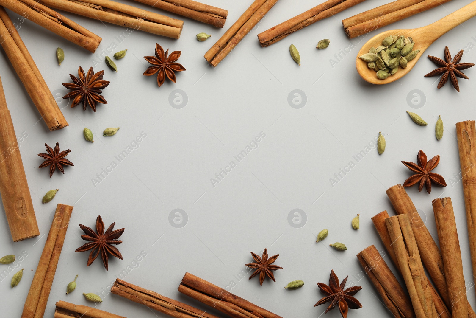 Photo of Frame made of cinnamon sticks, star anise and cardamom pods on light grey background, flat lay