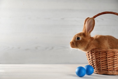 Photo of Cute bunny, basket and Easter eggs on white table. Space for text
