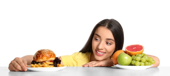Photo of Woman choosing between fruits and burger with French fries on white background
