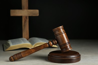 Photo of Judge gavel, bible and wooden cross on light grey table against black background