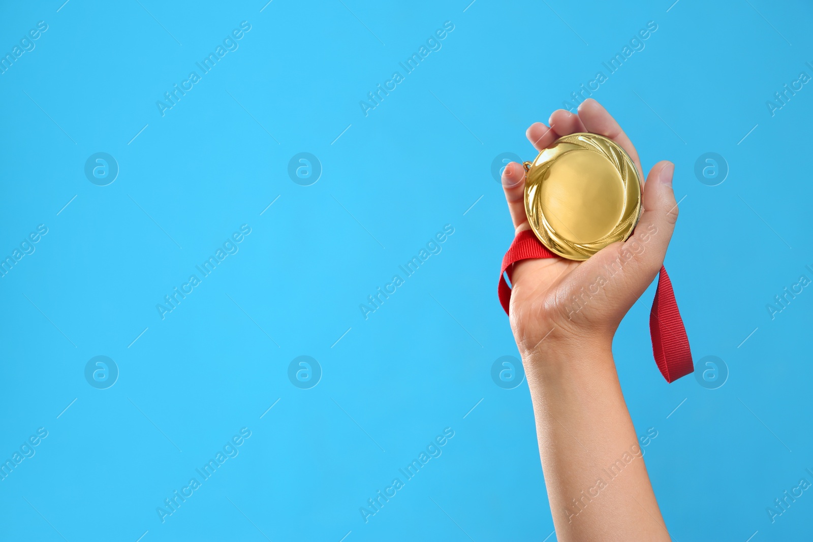 Photo of Woman holding gold medal on light blue background, closeup. Space for text