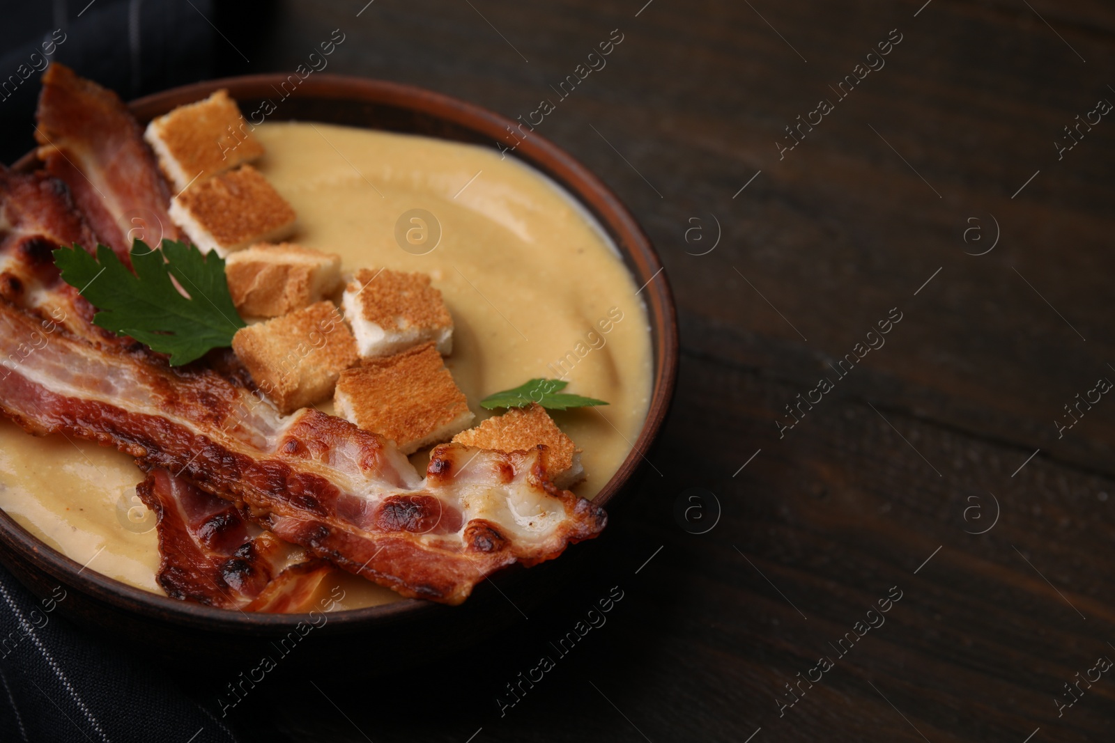 Photo of Delicious lentil soup with bacon and parsley in bowl on wooden table, closeup. Space for text