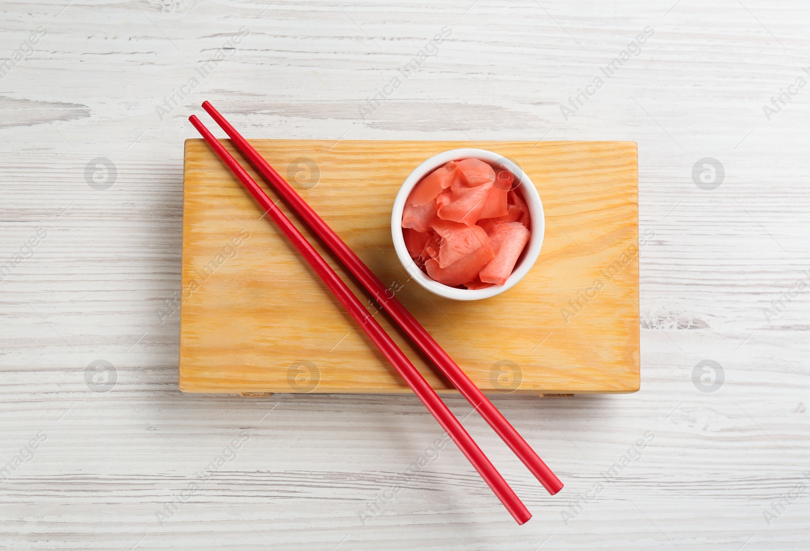 Photo of Spicy pickled ginger and chopsticks on white wooden table, top view