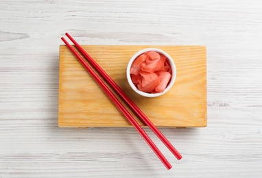 Photo of Spicy pickled ginger and chopsticks on white wooden table, top view