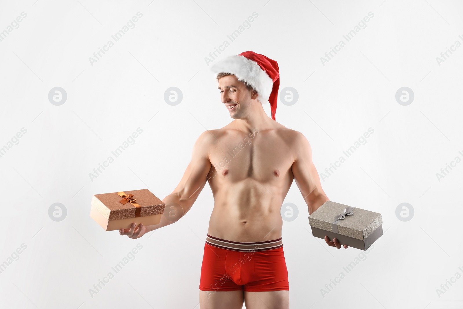 Photo of Young muscular man in Santa hat with gift boxes on white background