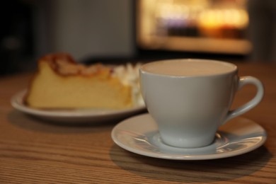 Photo of Cup of aromatic coffee and delicious dessert on wooden table in cafe, closeup