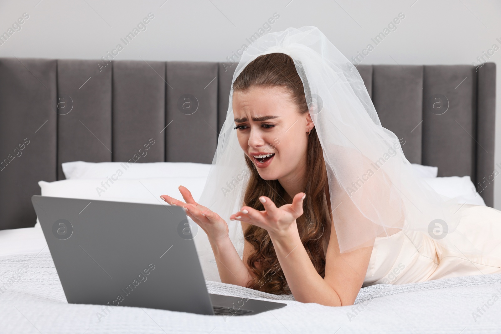 Photo of Emotional bride with laptop on bed in bedroom