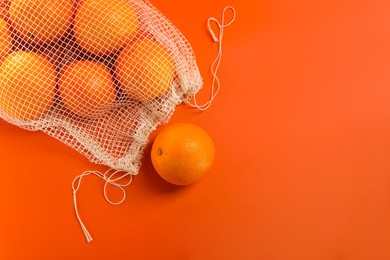 Net bag with fresh oranges on color background, top view. Space for text