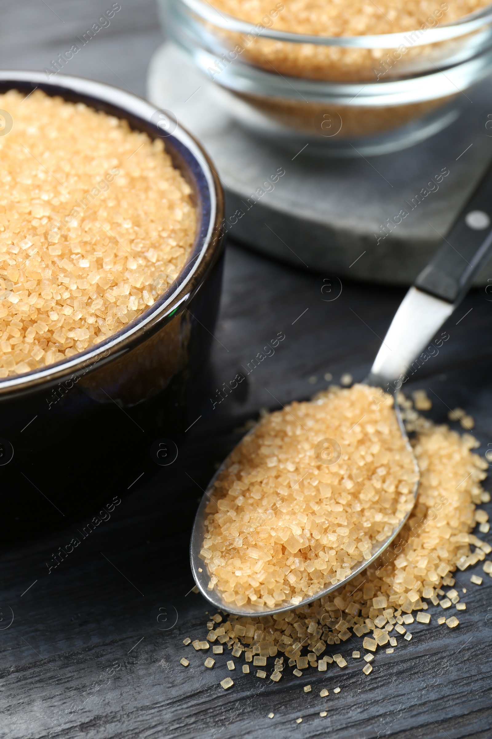 Photo of Brown sugar in bowl and spoon on black wooden table, closeup