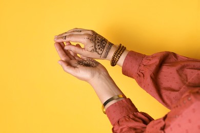 Woman with beautiful henna tattoos on hands against yellow background, closeup. Traditional mehndi