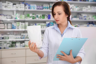 Photo of Professional pharmacist with clipboard and prescription in modern drugstore
