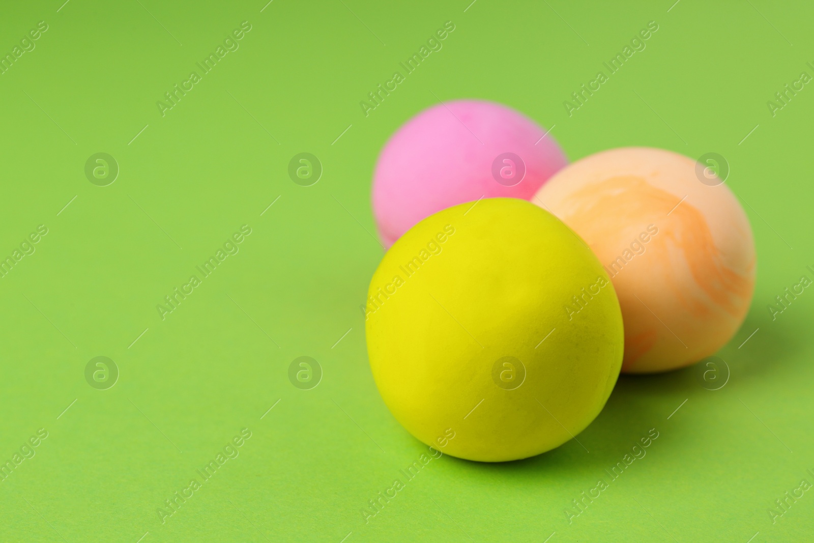 Photo of Different color play dough balls on light green background, closeup. Space for text