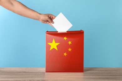 Image of Man putting his vote into ballot box decorated with flag of China against light blue background, closeup