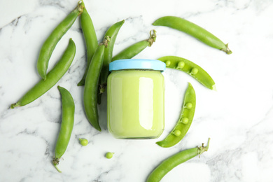 Photo of Baby food in jar and fresh green peas on white marble table, flat lay